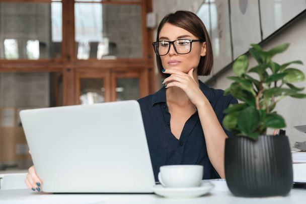 Calm woman in eyeglasses working with laptop computer - Fotó, kép