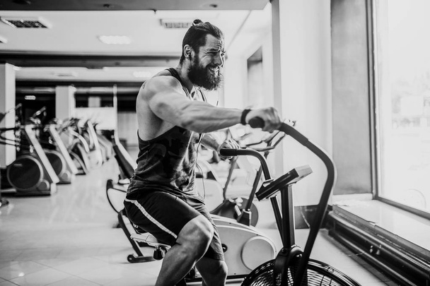 un joven que usa bicicleta estática en el gimnasio. Fitness masculino usando bicicleta neumática para entrenamiento cardiovascular en el gimnasio crossfit
. - Foto, imagen