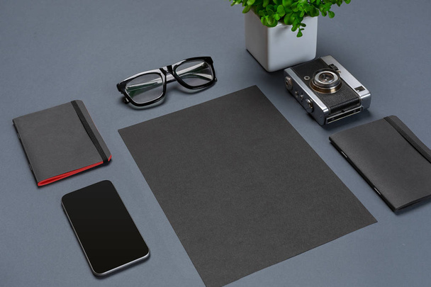 Un conjunto de accesorios de oficina negro, gafas, flor verde e inteligente sobre fondo gris
 - Foto, imagen