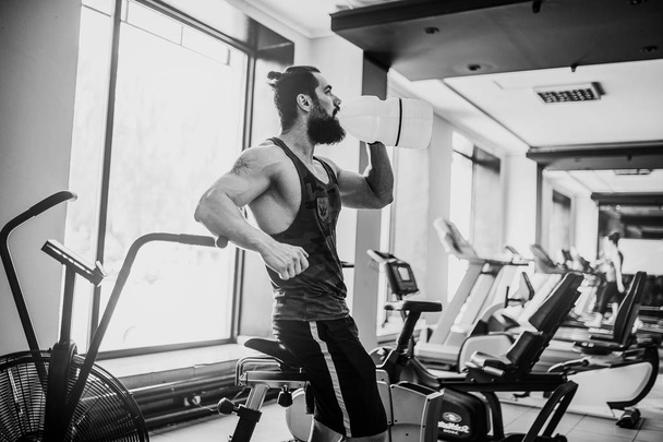 guy relaxing after workout and hold or drink water from big bottle in gym - Foto, imagen