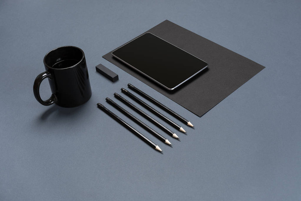 Plat leggen van lege zwart papier vel, zwarte briefpapier items en koffiekopje op grijze bureaublad. Mock up - Foto, afbeelding