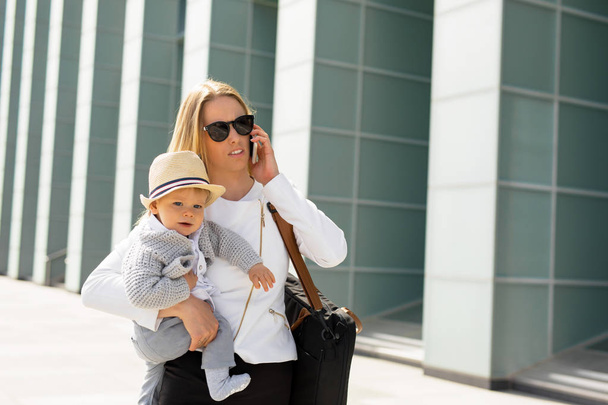 Mère prospère dans les affaires marchant avec bébé dans ses mains et parlant sur téléphone portable
 - Photo, image