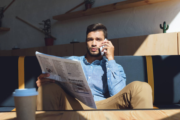 man with smartphone reading newspaper - Фото, изображение