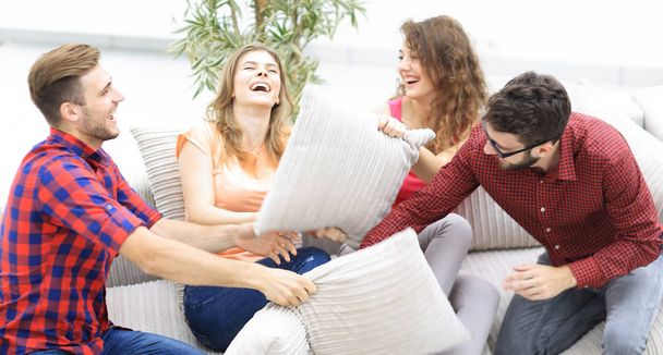 cheerful friends playing with the pillows sitting on the couch - Photo, image