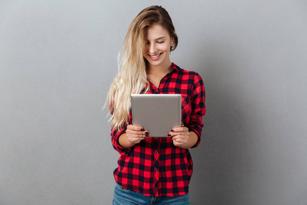 Cheerful young blonde woman chatting by tablet computer. - 写真・画像