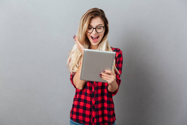 Surprised young blonde woman chatting by tablet computer. - 写真・画像