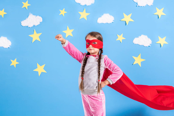 Menina loira de seis anos vestida como super-herói se divertindo em casa. Criança no fundo da parede azul brilhante
. - Foto, Imagem
