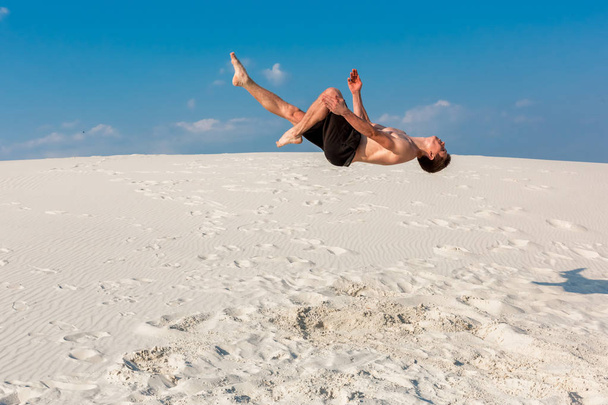 Porträt eines jungen Parkour-Mannes, der Flip oder Salto auf dem Sand macht. - Foto, Bild