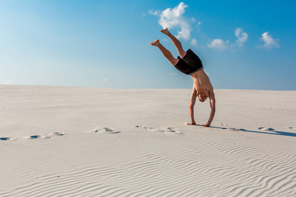 Sportieve jongeman wilt doen acrobatische oefeningen op het zand in de buurt van rivier - Foto, afbeelding