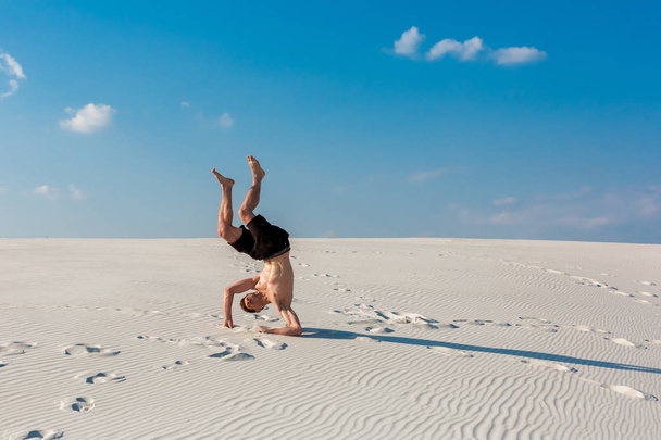 Młody człowiek sportowy ma ćwiczeń akrobatycznych na piasku w pobliżu rzeki - Zdjęcie, obraz
