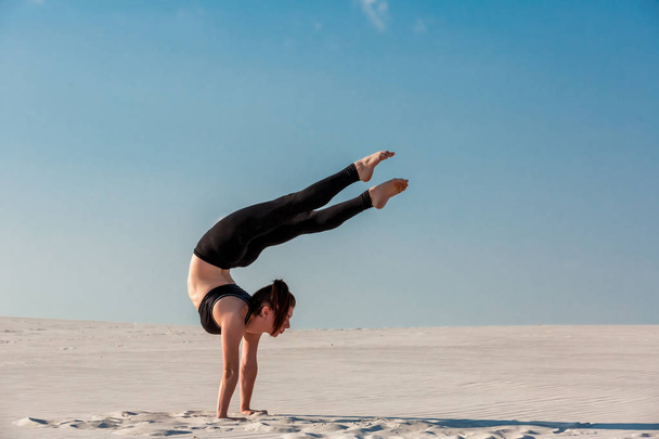 若い女性の白い砂と明るい青い空とビーチで逆立ちの練習 - 写真・画像