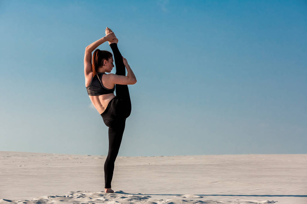 Молодая стройная женщина занимается гимнастикой на пляже с белым песком под голубым небом
. - Фото, изображение