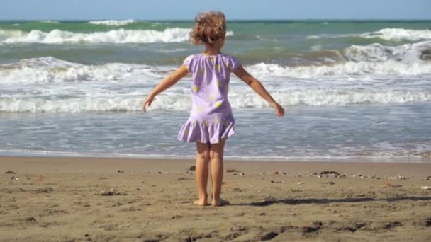 Concept of freedom little girl with open arms in front of ocean with big waves slow motion - Footage, Video