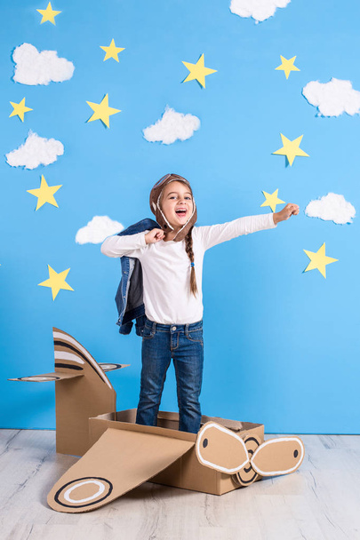 Маленька дівчинка мрійник грає з картонним літаком в студії з блакитним небом і білими хмарами фону
. - Фото, зображення