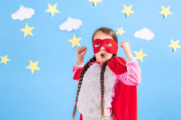 Little child plays superhero. Kid on the background of bright blue wall with white clouds and stars . Girl power concept. - Fotó, kép