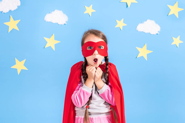 Little child plays superhero. Kid on the background of bright blue wall with white clouds and stars . Girl power concept. - Photo, Image