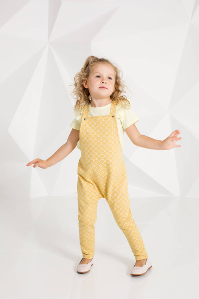 Beautiful little girl with blond hair, in yellow overalls on white background - Photo, Image