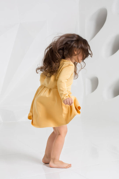Mała dziewczynka sobie żółta sukienka taniec w studio białym tle. - Zdjęcie, obraz