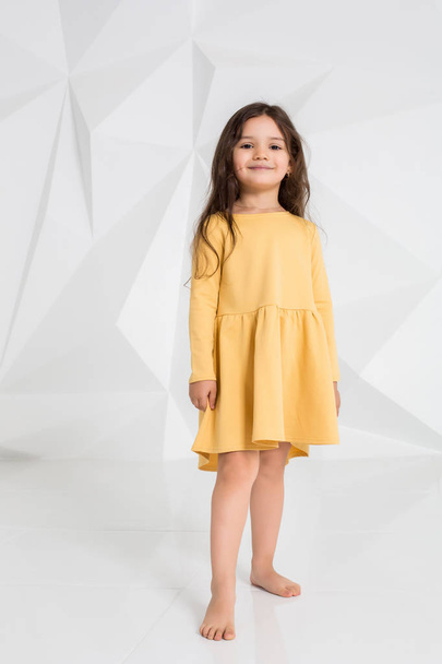 Маленька дівчинка в жовтій сукні танцює в студії на білому тлі
. - Фото, зображення