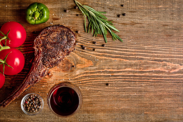 Barbecue droge leeftijd rib van rundvlees met groenten en een glas rode wijn close-up op houten achtergrond - Foto, afbeelding