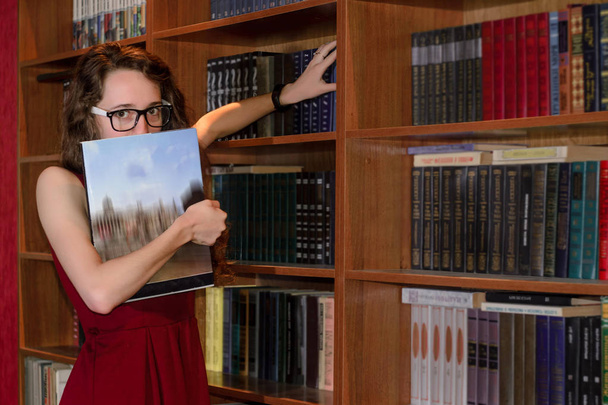 Mädchen versteckt Gesicht hinter Buch in Bibliothek. - Foto, Bild