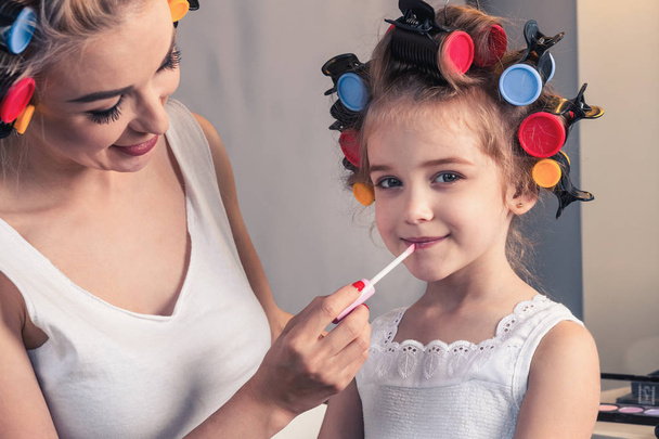 Pretty mother and her daughter having fun with lipstick while do - 写真・画像