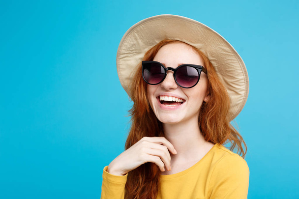 旅行の概念 - トレンディな帽子とサングラス笑みを浮かべて肖像若い美しい魅力的な redhair 女の子を閉じる。青いパステル背景。コピー スペース. - 写真・画像