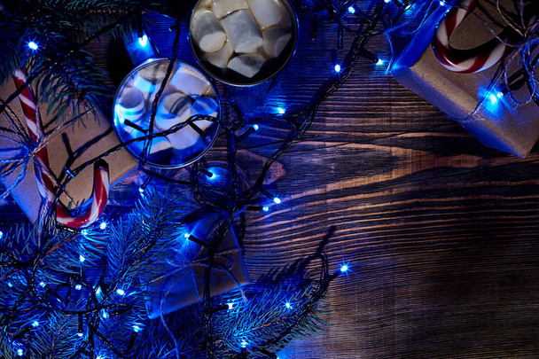 Bebida caliente de Navidad. Cacao con malvavisco, guirnalda y ramas de abeto sobre un fondo de madera. Vista superior
 - Foto, Imagen