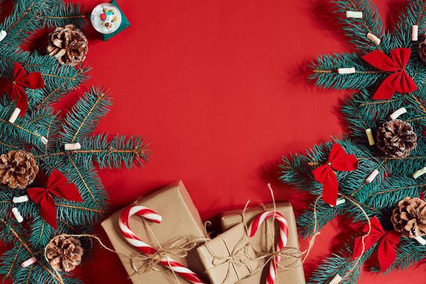 Kerst samenstelling van dennenappels, vuren takken en stapel geschenkdozen op rode achtergrond - Foto, afbeelding