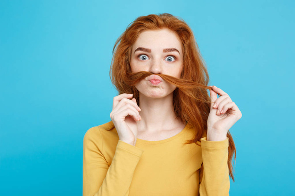 Headshot πορτρέτο του happy τζίντζερ κόκκινα μαλλιά κορίτσι μιμείται να είναι άνθρωπος με ψεύτικο μουστάκι μαλλιά. Παστέλ μπλε φόντο. Χώρο αντίγραφο. - Φωτογραφία, εικόνα