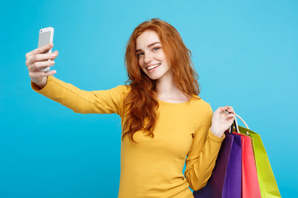 Koncepcja zakupy - bliska portret młody piękny redhair atrakcyjna dziewczyna uśmiechając się, patrząc na kamery z biała torba na zakupy i selfie. Niebieskim tle Pastel. Miejsce. - Zdjęcie, obraz