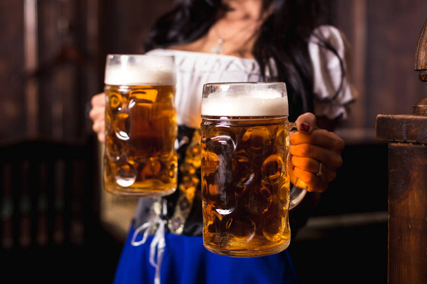 Jovem sexy Oktoberfest garçonete, vestindo um vestido tradicional da Baviera, servindo canecas de cerveja grandes no bar
. - Foto, Imagem