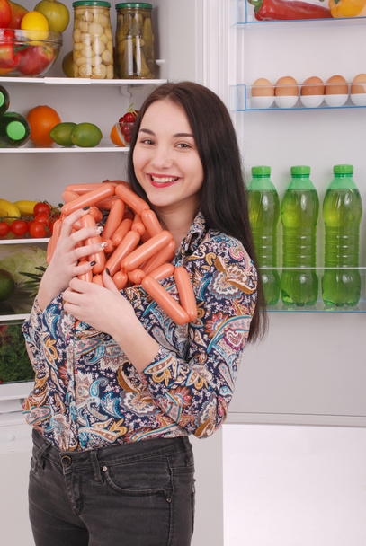 Young girl holds sausages on the refrigerator background - Φωτογραφία, εικόνα