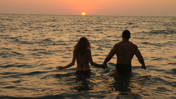 Sziluettek a terhes nők bikini és romantikus izmos ember. a testépítő ölelést, megcsókolja a feleségét és a stroke a hasát. a háttérben a tengeri naplemente. 4 k. lassú mozgás - Felvétel, videó