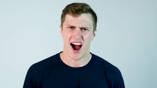 Een jonge man schreeuwt tegen de camera met zwart t-shirt en een grijze achtergrond. Slow motion - Video