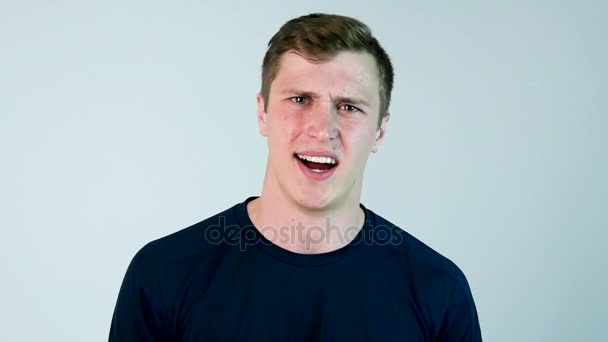 An young man yells at the camera with black t-shirt and grey background. Slow motion - Footage, Video