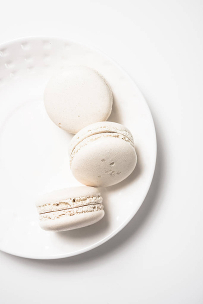 Three beige white macaroon cookies on plate - Фото, зображення