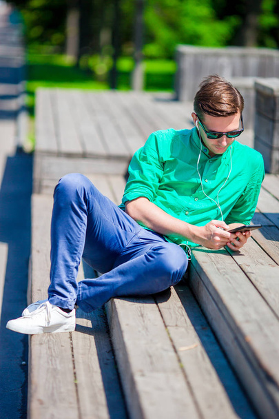 Νεαρός με smartphone σε εξωτερικούς χώρους στο πάρκο ο άνθρωπος χρησιμοποιώντας κινητό smartphone. - Φωτογραφία, εικόνα