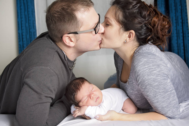 Щаслива сім'я з новонародженою дитиною на ліжку в кімнаті
 - Фото, зображення