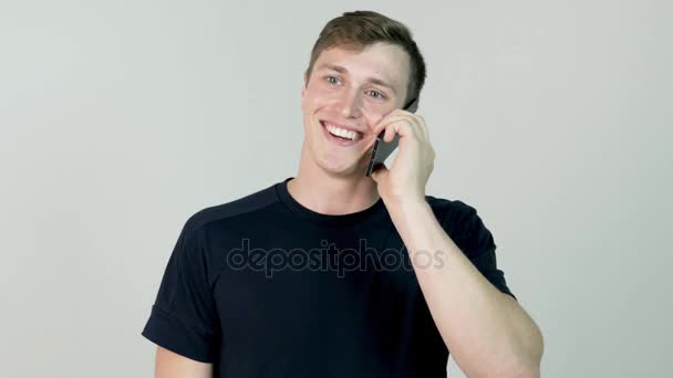 Portrait of a smiling latin adult man speaking on cellphone on white background. Young casual man talking on the phone against light wall - Кадры, видео