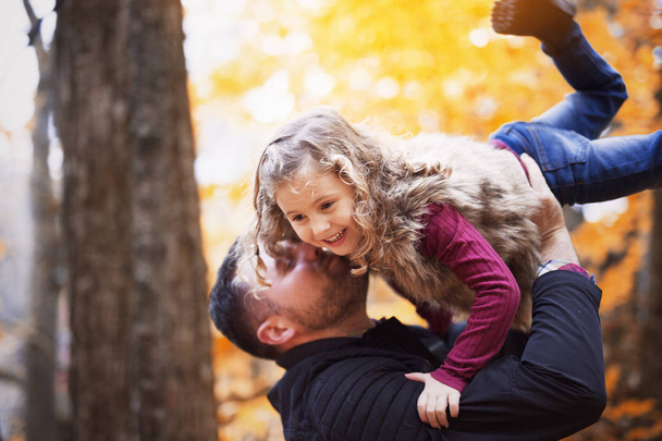 Little adorable girl with happy father in autumn park outdoors - Fotó, kép