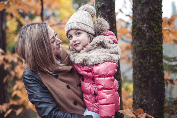 Porträt einer lächelnden jungen Frau mit einem kleinen Mädchen im Herbst - Foto, Bild