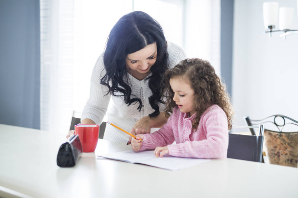 Beautiful school girl doing homework with mother at home - 写真・画像