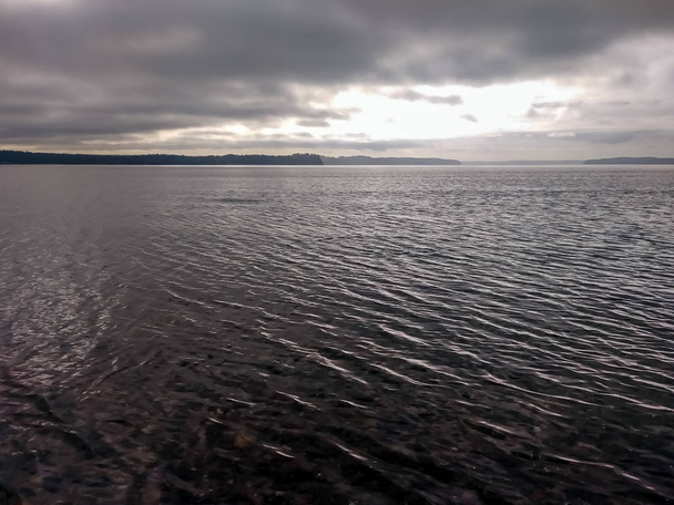 grijze rimpelingen op het water en bewolkte hemel - Foto, afbeelding