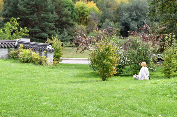 Kobieta siedzi na trawnik w parku miejskim - Zdjęcie, obraz