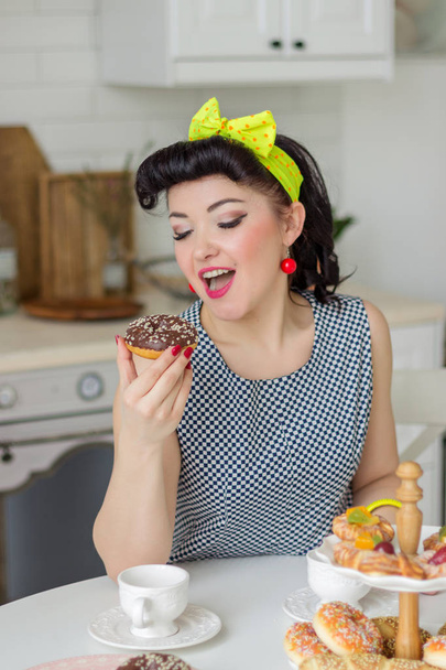 pin up girl emotionally eating a donut in the kitchen at the table - Foto, imagen