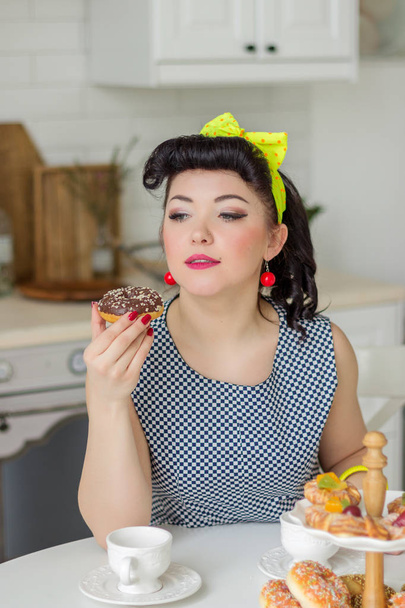 pin up girl emotionally looks at donut in the kitchen at the table - Fotoğraf, Görsel