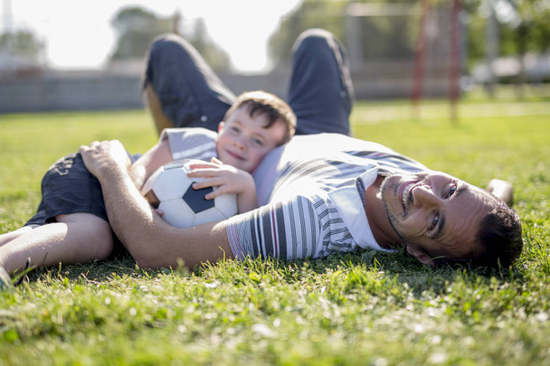 man with child playing football on field - Foto, imagen