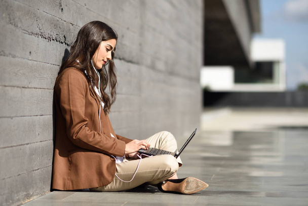 Joven mujer de negocios sentada en el suelo mirando su compu portátil
 - Foto, imagen
