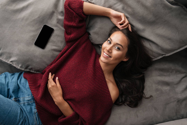 Smiling asian woman in sweater lying on a couch - Foto, Imagem